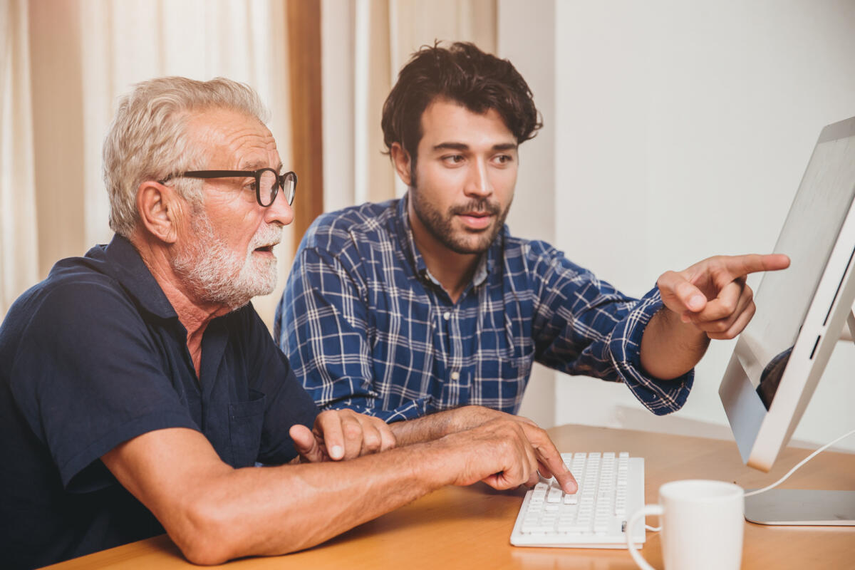 A Bari arriva il ‘nipote in affitto’. Senex: un sogno che si realizza - young man or son teaching his grandfather elderly dad learning to using computer at home.