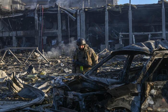 A Ukranian serviceman looks at a destroyed vehicle in the grounds of the Retroville shopping mall following a Russian missile attack in Kyiv on March 21, 2022. - At least six people were killed in the overnight bombing of a shopping centre in the Ukrainia