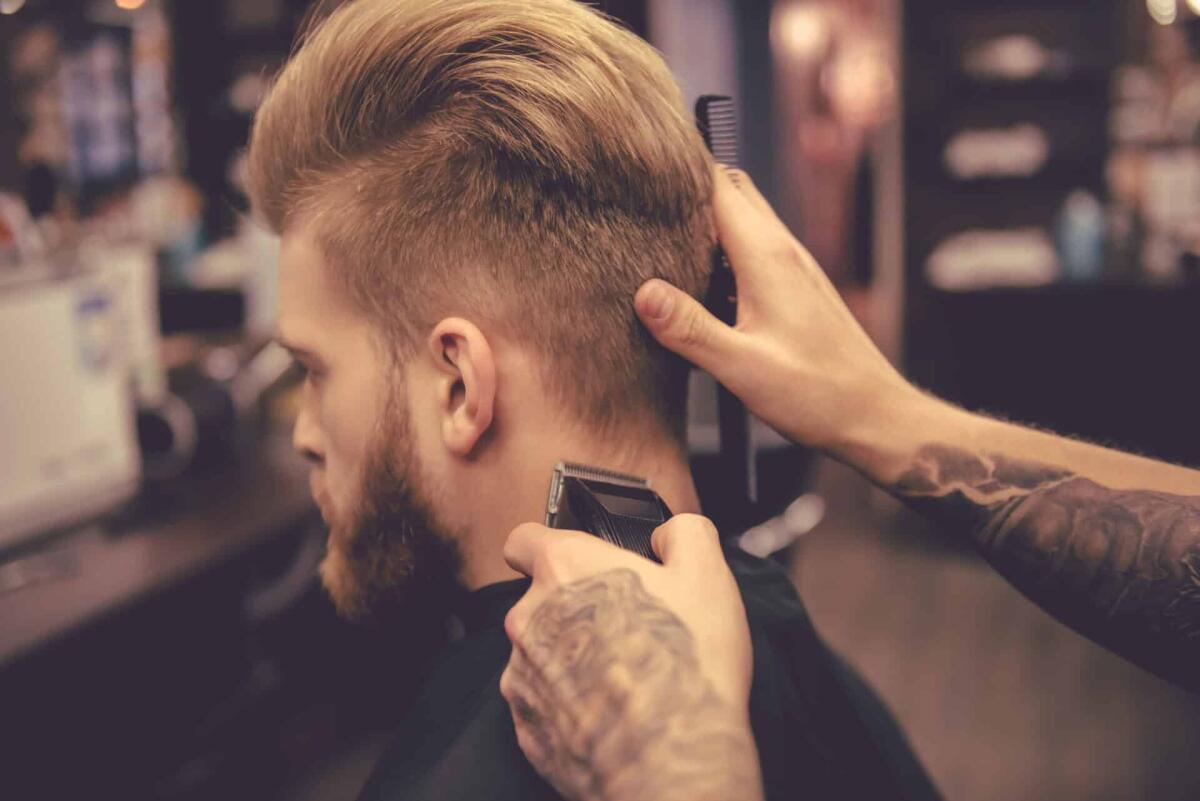 Tagliacapelli professionali: i migliori per un taglio ottimo - Back view of handsome bearded man getting haircut by hairdresser at the barbershop