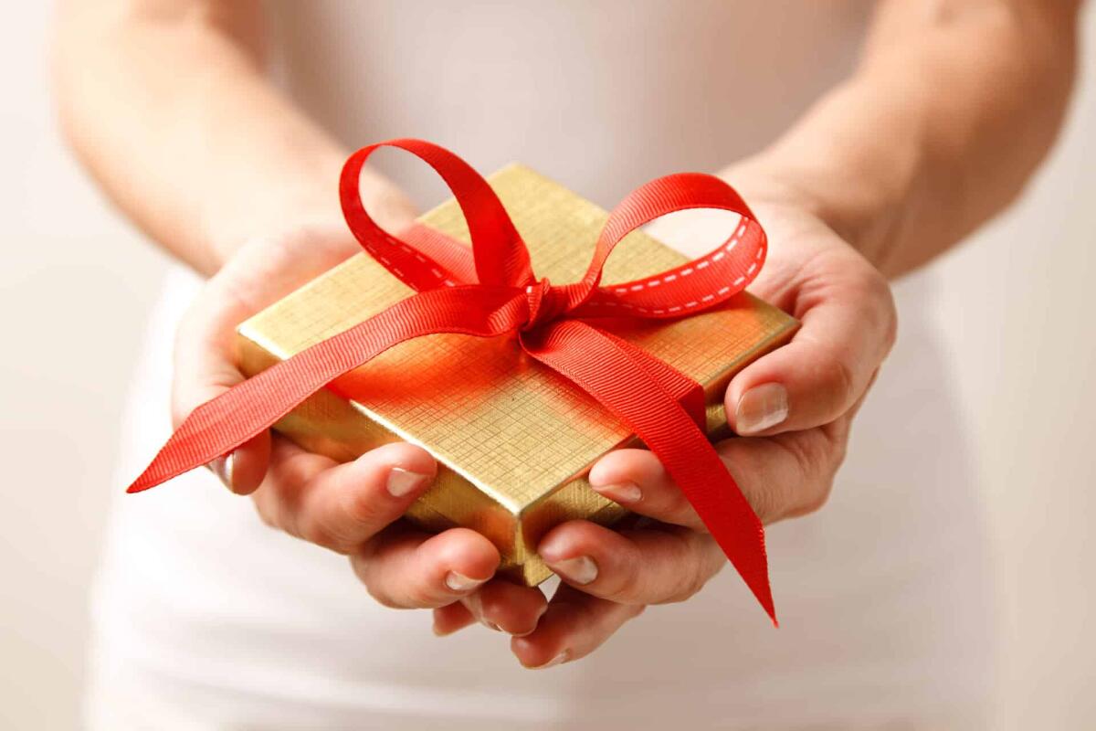 Idee regalo per Natale da piccole aziende italiane - Woman holding a gift box in a gesture of giving.