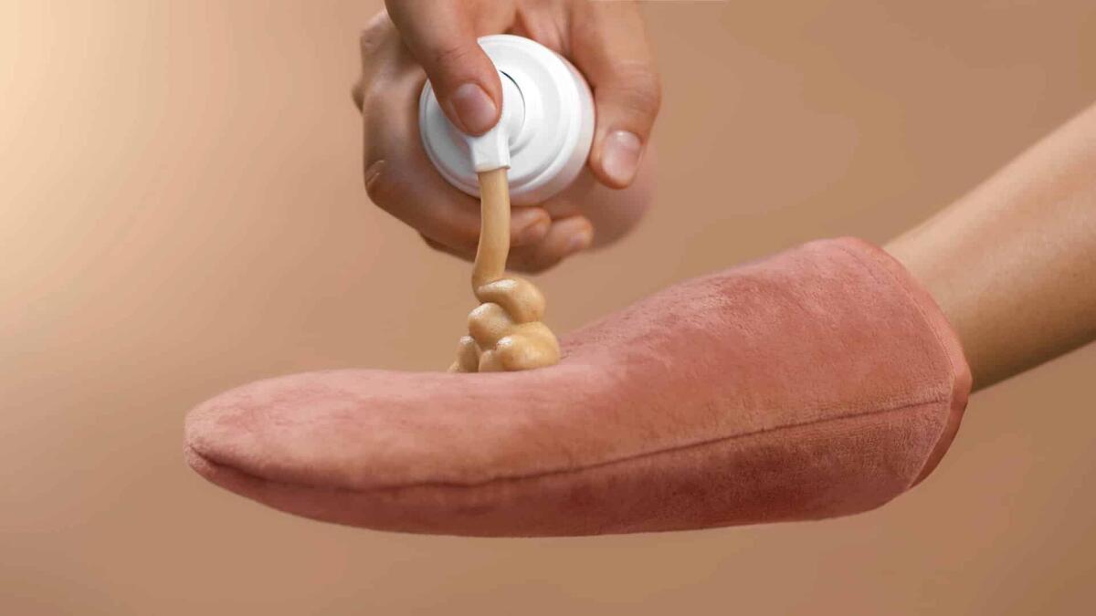 Crema autoabbronzante corpo 2023: come scegliere la migliore - Dosing bronzing lotion or tanning cream from a flask with a doser to a pink tan applicator glove. High quality close-up studio photo image beige background.