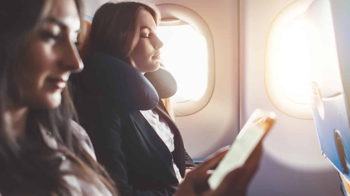 Cuscini da viaggio: utilizzo, modelli e dove comprarli - Two females going on business trip by plane. A woman reading an e-book on a smartphone.