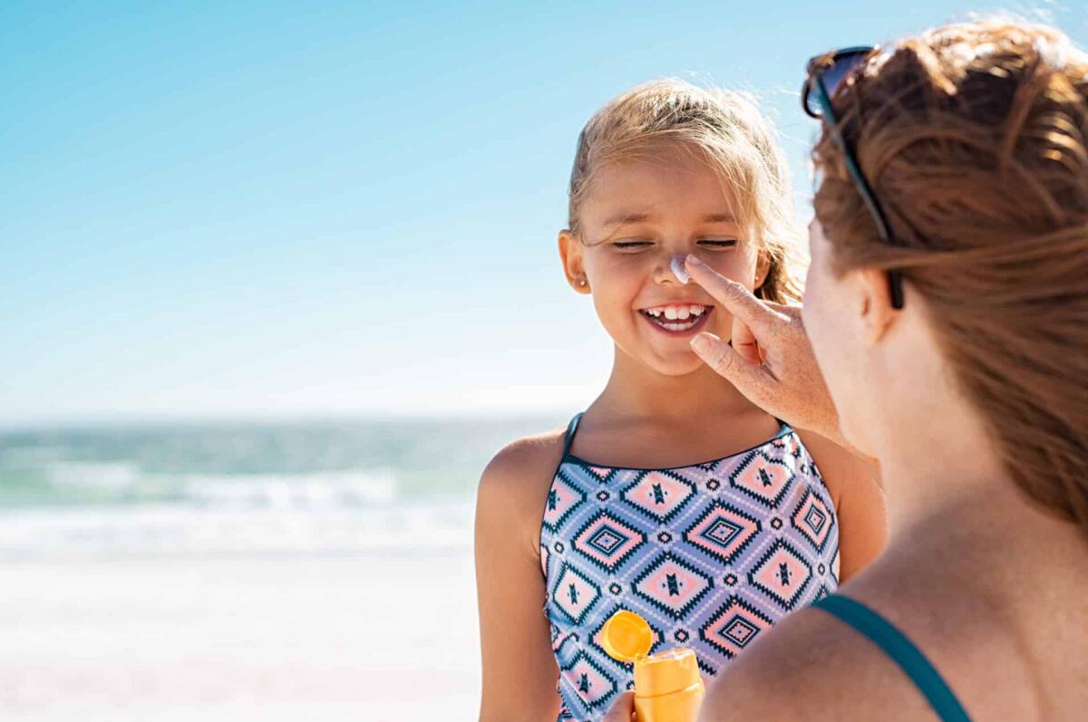 Creme solari ecosostenibili: quale scegliere? - Young mother applying protective sunscreen on daughter nose at beach. Woman hand putting sun lotion on child face. Cute little girl with sunblock at seaside with copy space.