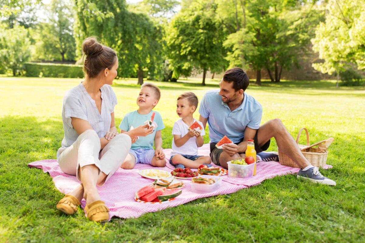 Kit picnic: il set da avere per una scampagnata perfetta - family, leisure and people concept - happy mother, father and two little sons having picnic and eating watermelon at summer park