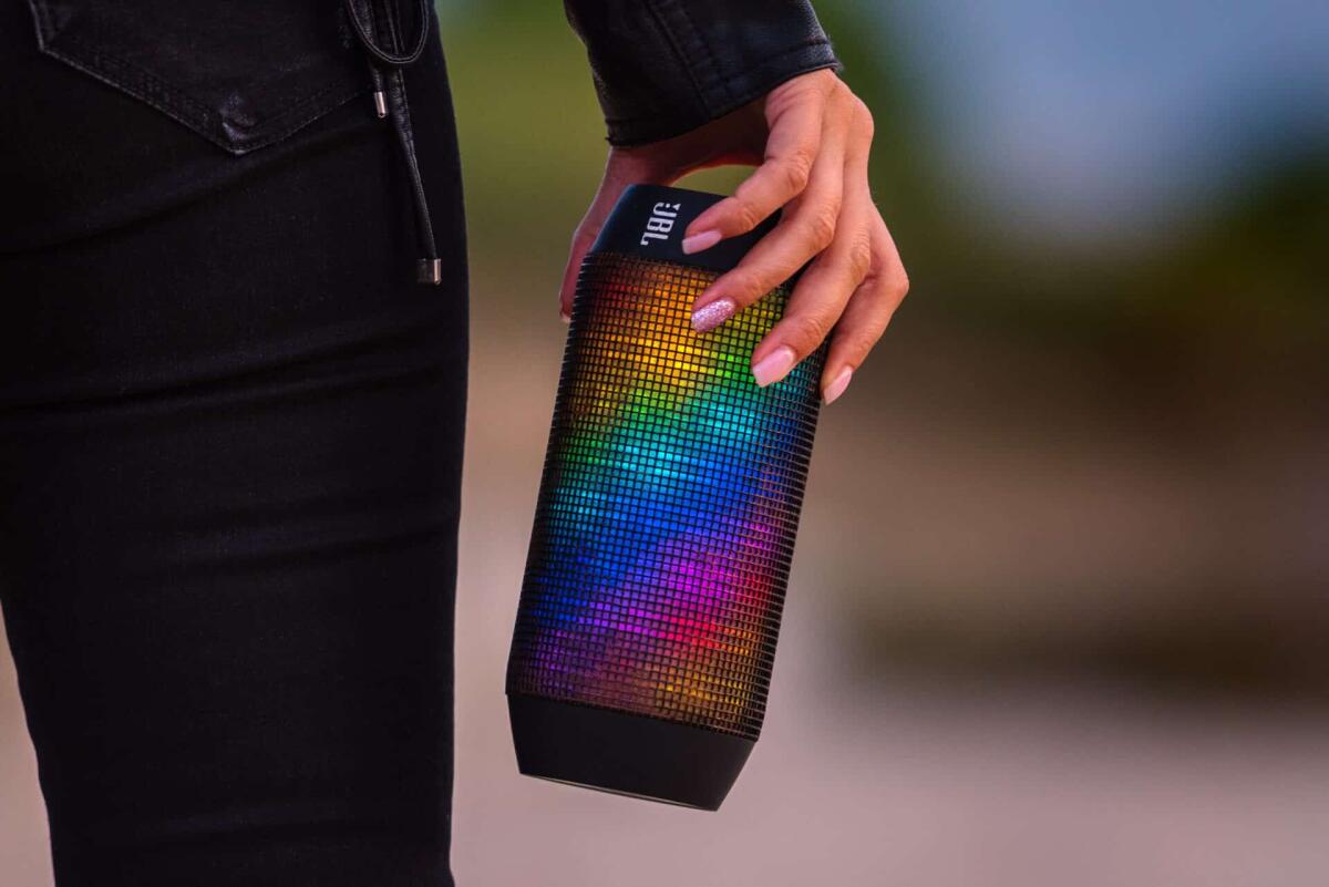 Altoparlanti Bluetooth, quali scegliere? Modelli e prezzi - Close up photo of woman's hand holding LED portable JBL multicolour wireless bluetooth speakers. Listening and enjoying the music outdoors. High quality photo