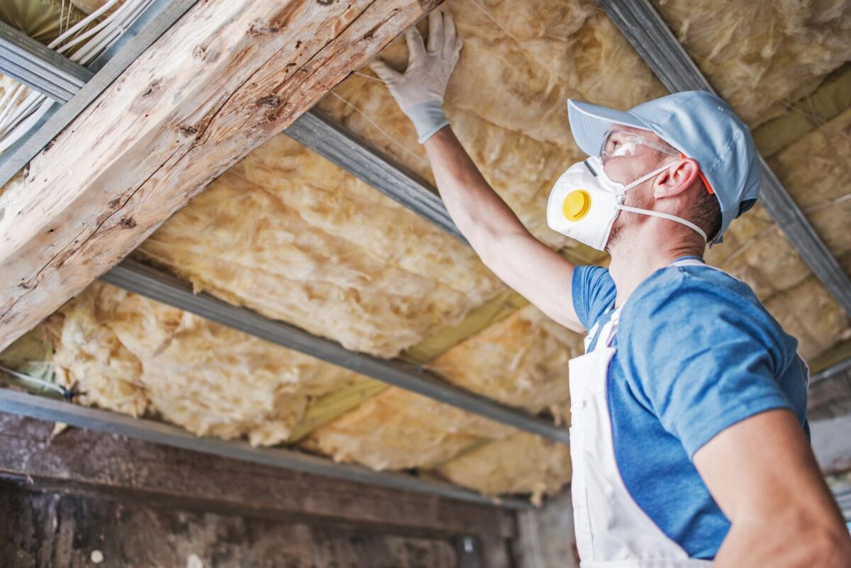 Isolamento del tetto, un’operazione fondamentale sotto tanti aspetti - Old Roof Insulation. Caucasian Construction Worker in His 30s Inspecting Aged Roof and Mineral Wool Insulator.
