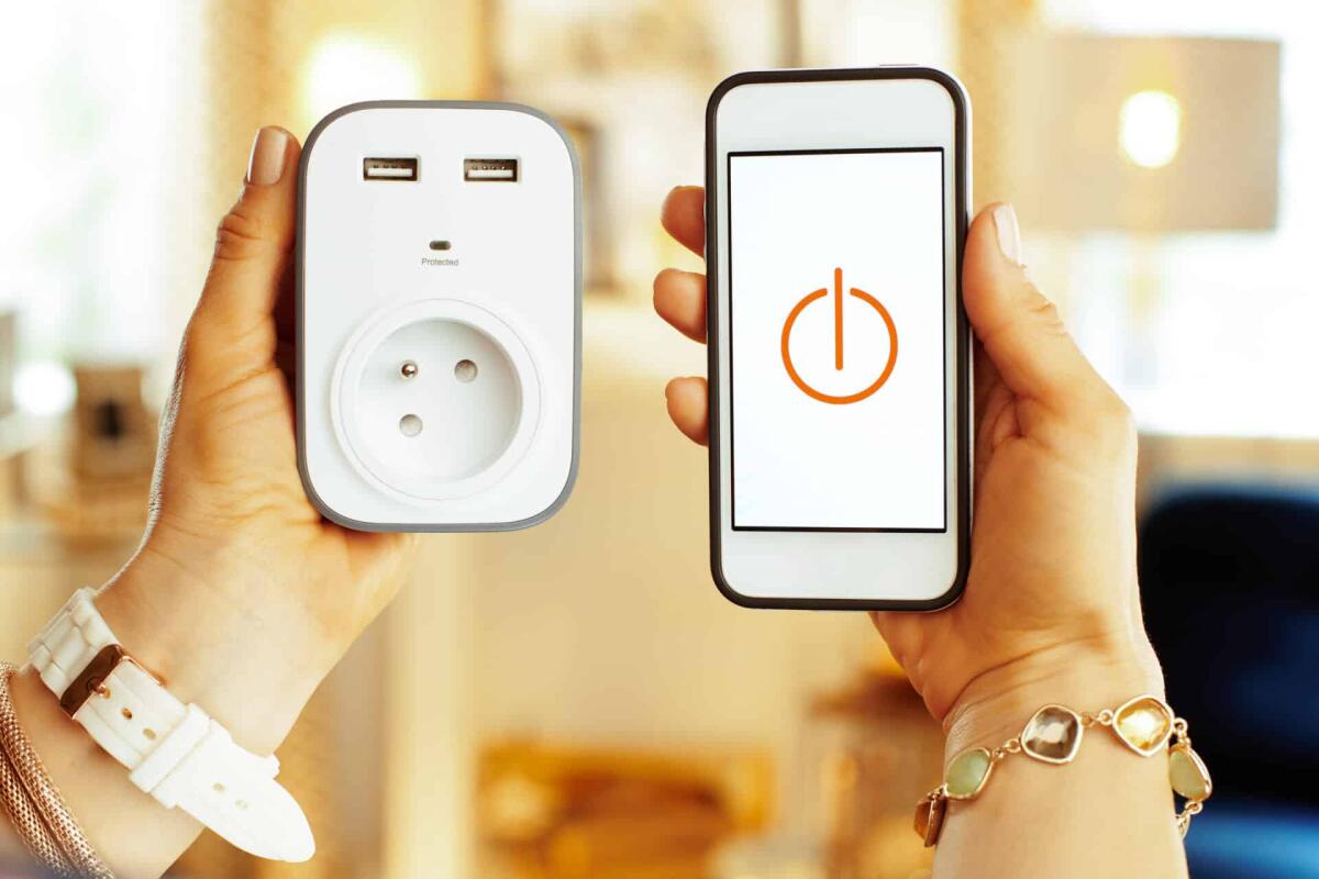 Presa smart WiFi: ecco le migliori per la domotica e per il risparmio energetico - Closeup on smartphone with smart home app and wifi smart plug in hands of modern woman in the house.
