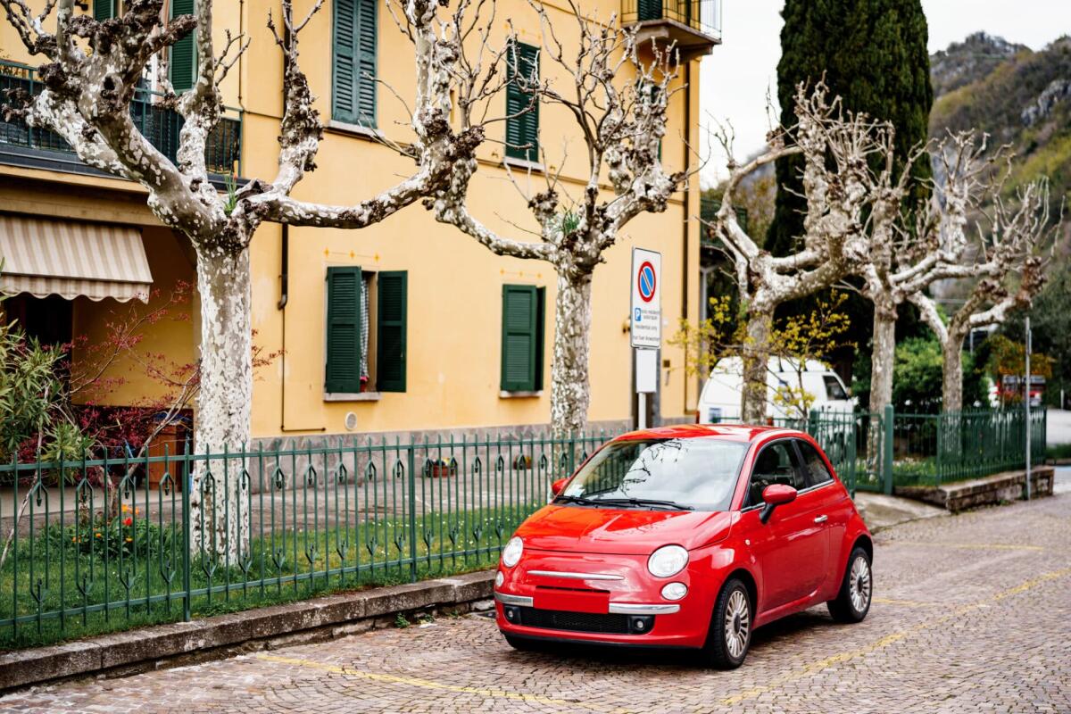 Come trovare la migliore auto FIAT per te: i fattori da valutare - A red Fiat 500 car parked outside a house with sycamore trees, or chinar in the garden, in Varena, Italy. High quality photo