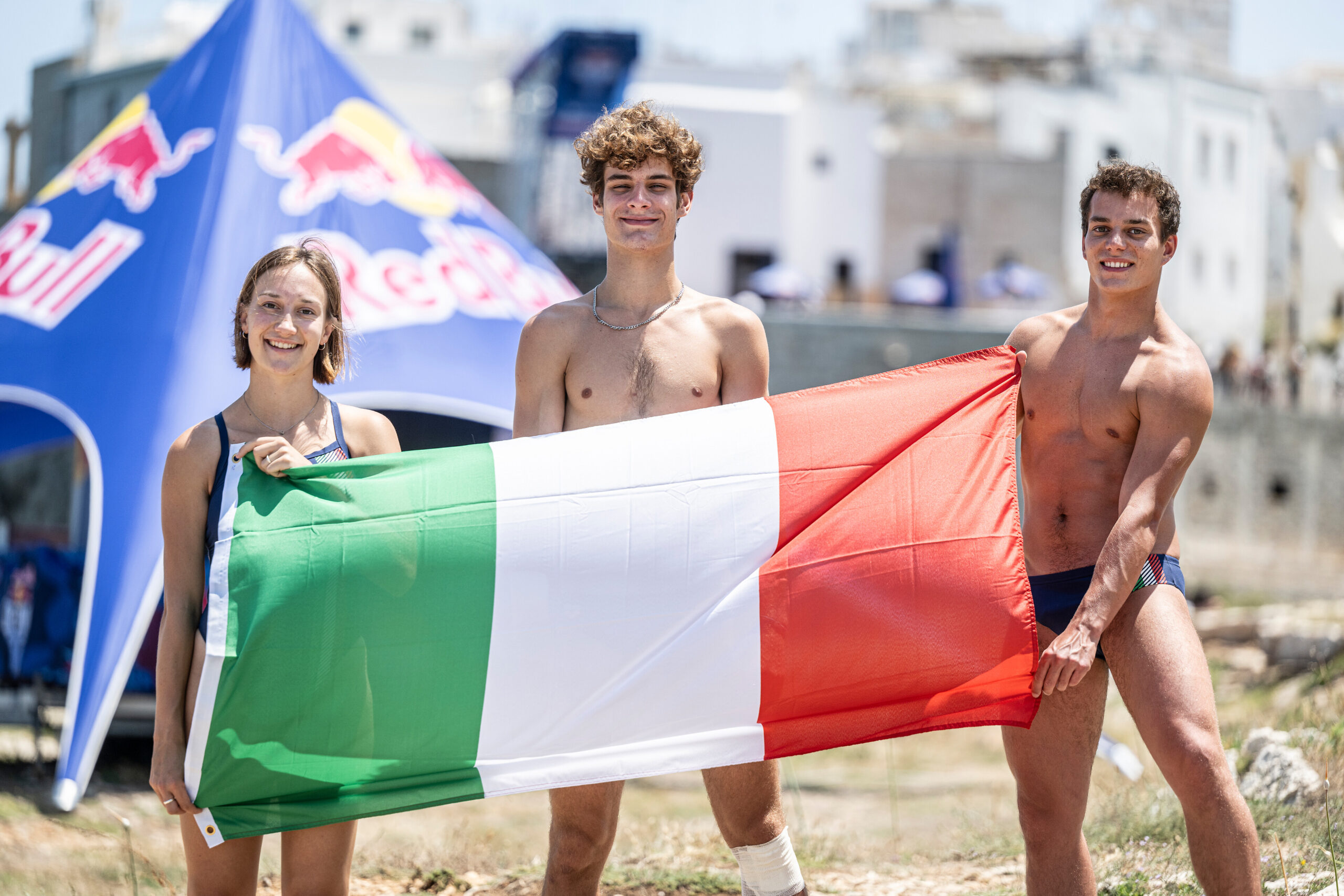 Italian divers (L-R) Elisa Cosetti, Andrea Barnaba and Davide Baraldi pose with their national flag during the training day of the third stop of the Red Bull Cliff Diving World Series in Polignano a Mare, Italy on June 30, 2023. // Dean Treml / Red Bull C